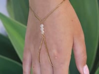 A slowly moving hand wearing a delicate gold hand chain with three small quartz crystal beads, shown worn against a blurred green background.