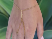 A slowly moving hand wearing a  delicate gold hand chain with a small cluster of citrine beads at the center, shown worn against a green leaf background.